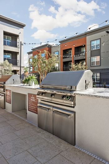 A row of outdoor stainless steel grills and ovens on a patio.